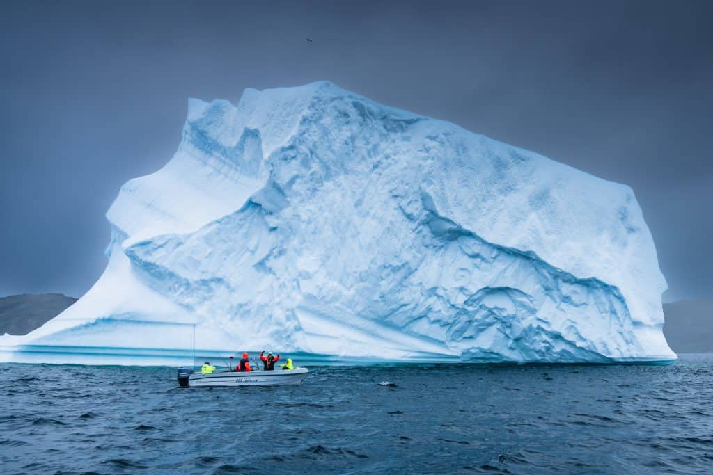 Large iceberg floating in cold Arctic waters with a small boat nearby.