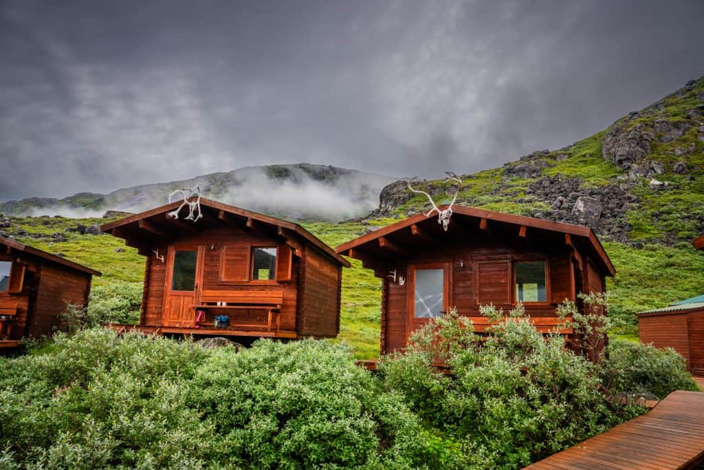 Two wooden cabins on a lush green hillside with misty mountains in the background.