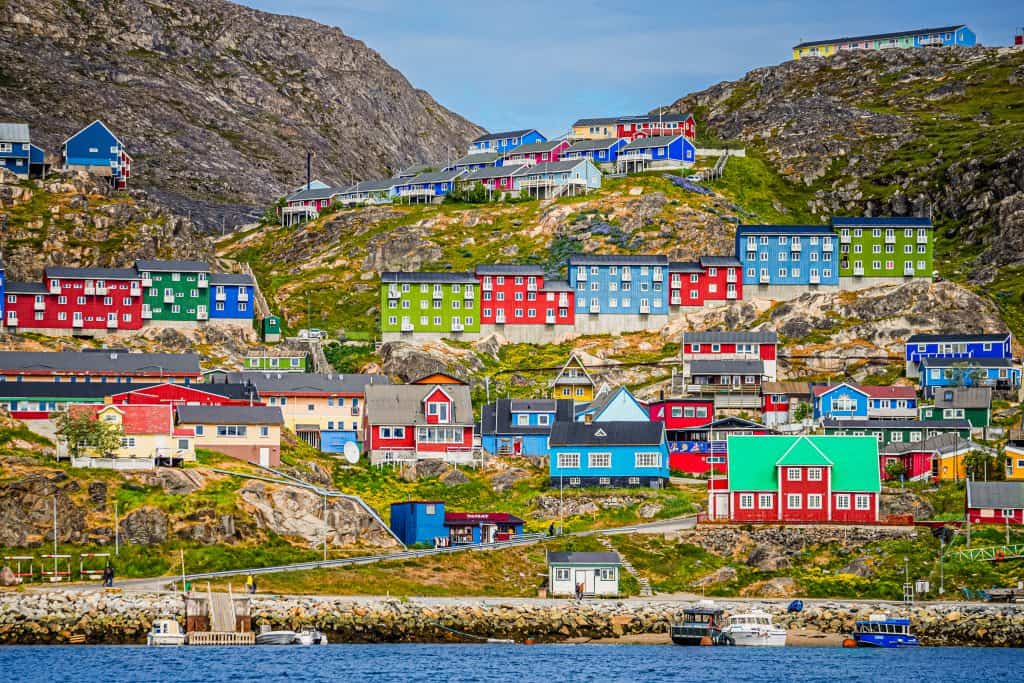 Vibrant houses on a steep hillside with mountains in the background in Greenland.