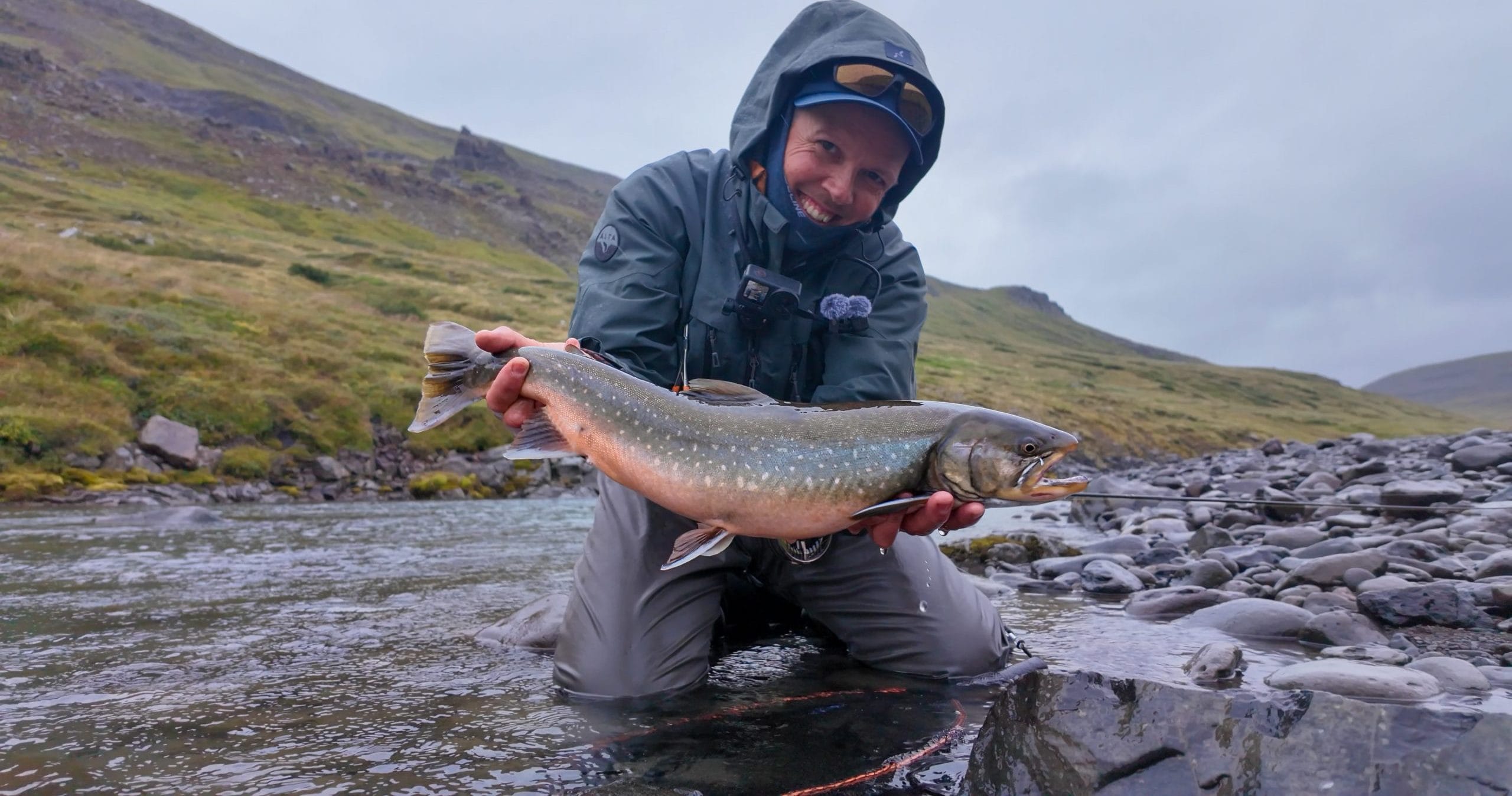 Angler holding a fish in the river during overcast weather.