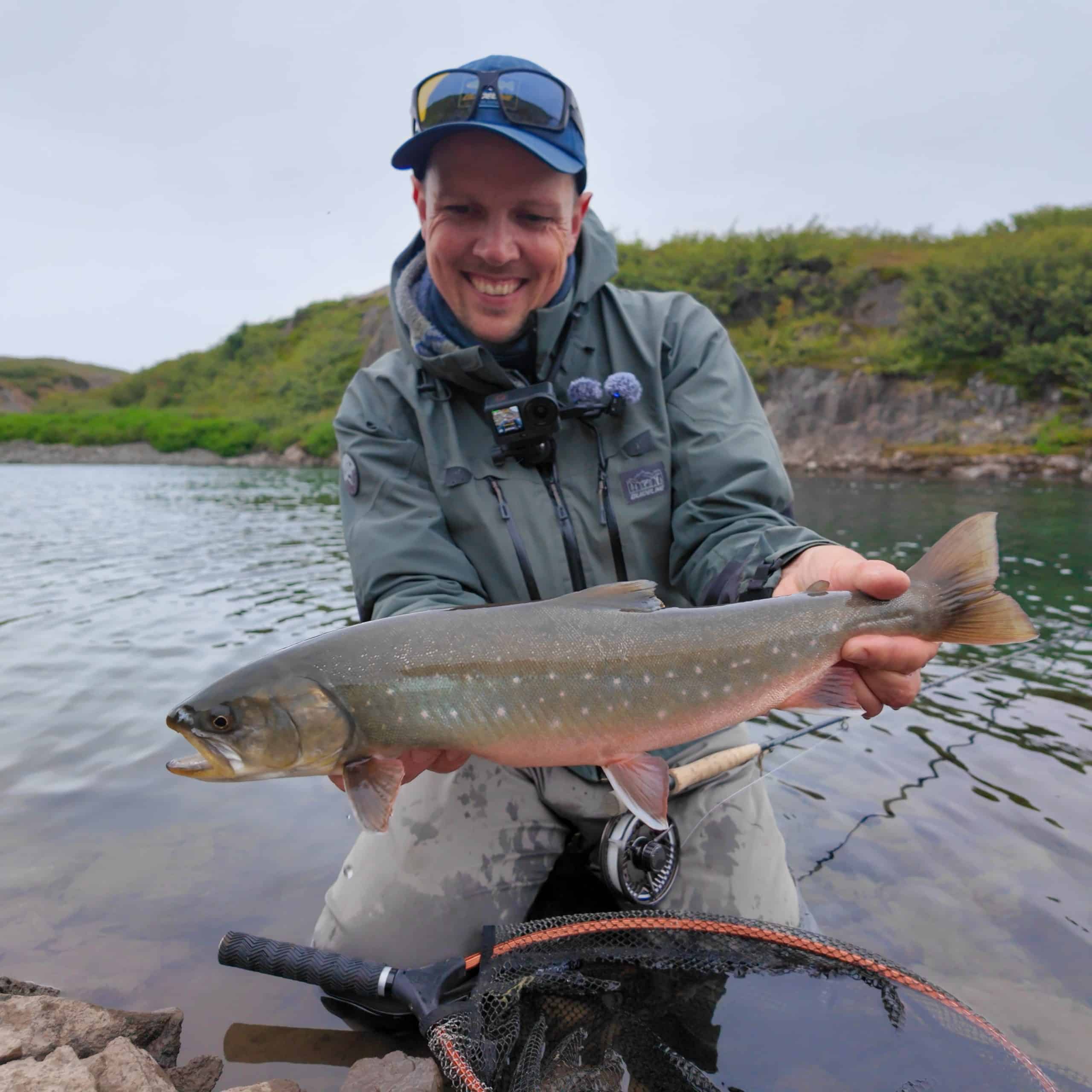 Angler holding a large fish in a river setting during fishing trip.