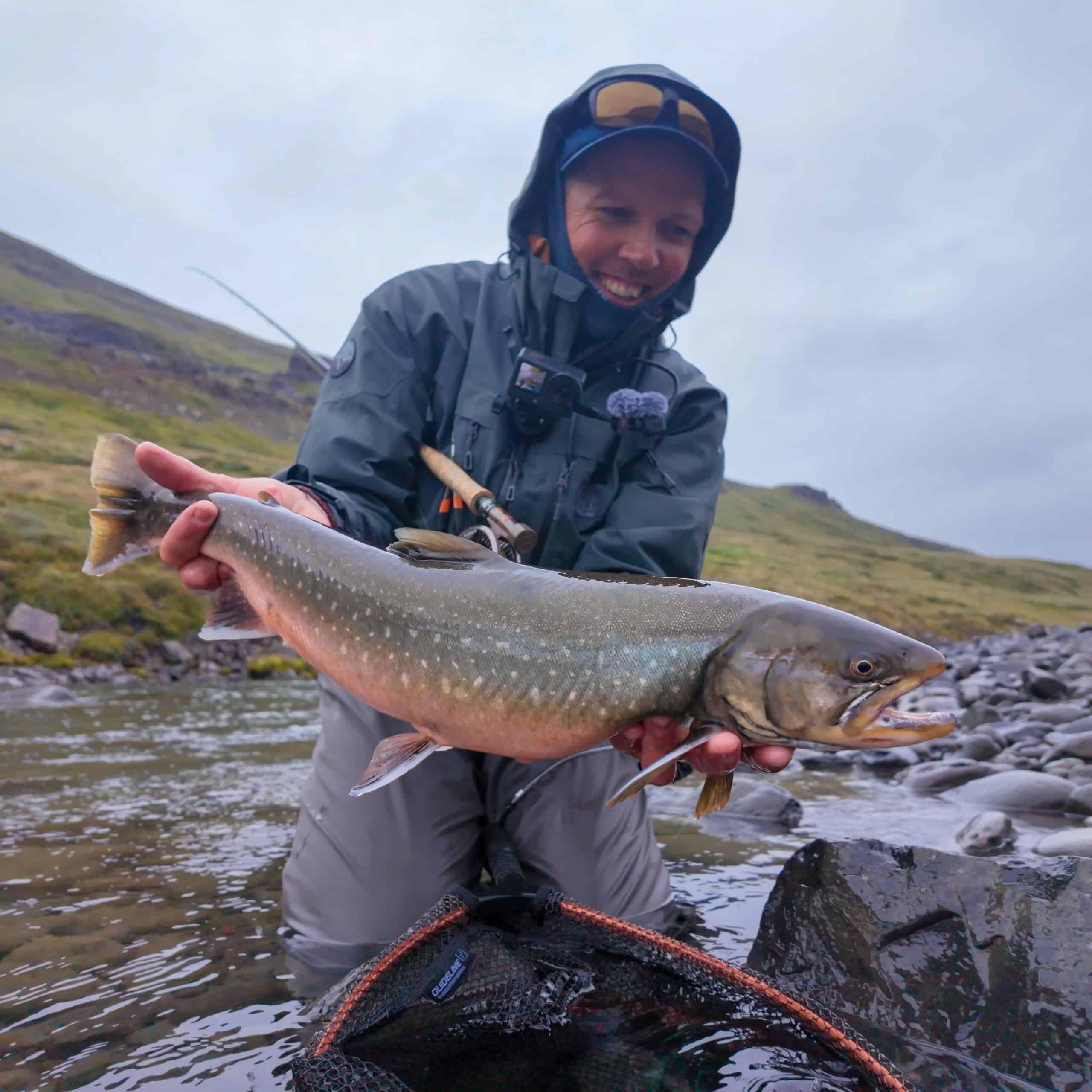 Angler holding a large fish in the river with scenic landscape.