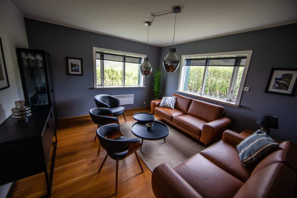 Contemporary living room with dark walls, wooden flooring, and large windows showing greenery.