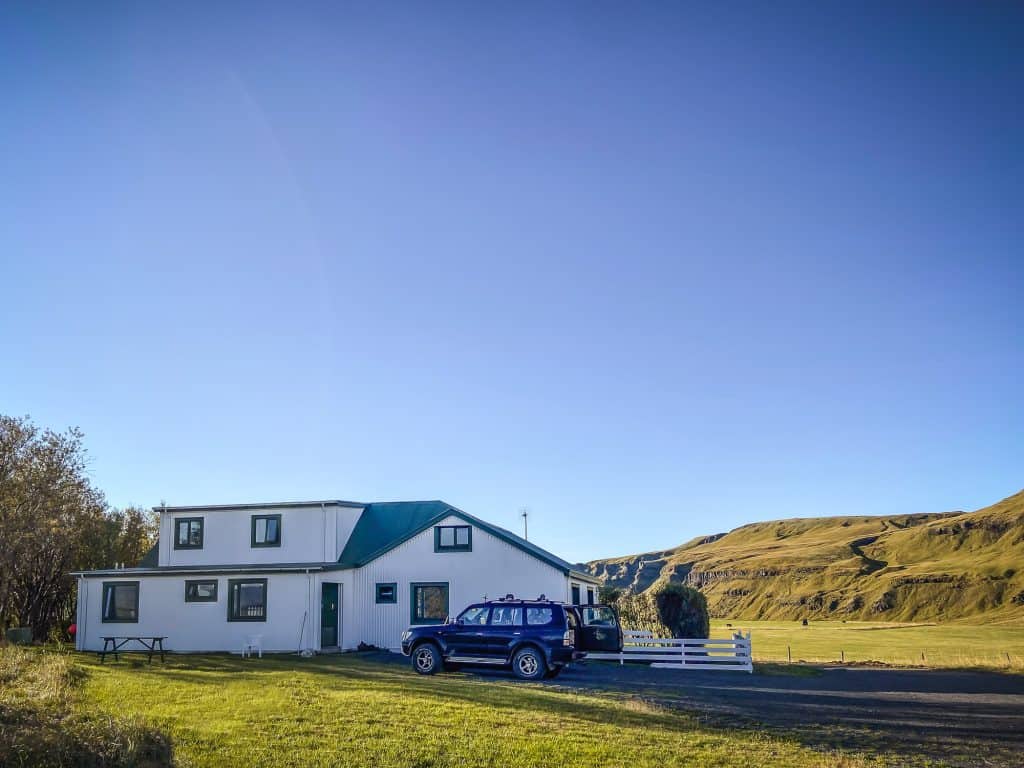 White lodge with blue roof and parked car in a lush green landscape.