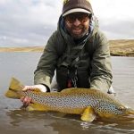 A fisherman displays a large, colorful rainbow trout in a peaceful natural river environment. Vibrant rainbow trout caught while fishing in a scenic outdoor river setting.