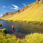Icelandic fishing scene with river and mountainous landscape for freshwater fish enthusiasts. Fishing in Iceland's scenic river surrounded by lush green hills and dramatic cliffs.