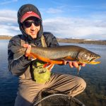 A fisherman holding a freshly caught rainbow trout in a pristine river with snow-capped mountains in the background. Casting a rainbow trout in a scenic river fishing outdoors on a bright day for freshwater game fish.