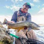 Man holding a big fish during a successful fishing trip by a river or lake. Large fish caught by a smiling angler in outdoor fishing environment.