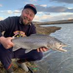 Happy man holding freshly caught rainbow trout during outdoor fishing adventure. Rainbow trout caught fishing at a scenic riverbank in open water.