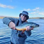 Happy angler holding a large fish during fishing adventure in natural waters. Vast fish caught on fishing trip in scenic outdoor setting with blue skies and water.