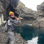 An adventurer engaged in outdoor fishing at a volcanic canyon, showcasing nature and sport fishing by the water's edge. High-altitude cliff fishing in rugged volcanic terrain. Angler caught a fish at a remote, rocky canyon by a clear water pool.
