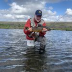 Enjoying a successful day of fishing with a freshly caught fish in a scenic river setting, perfect for freshwater fishing enthusiasts. Fresh caught fish being held by a smiling angler standing in a river, showcasing quality fishing and sustainable fish supply.