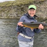 Smiling woman displaying her catch while fishing in a scenic river, highlighting outdoor fishing experiences and freshwater fish. Freshly caught fish held by a smiling angler on a riverbank, showcasing reliable fishing gear and successful catch.