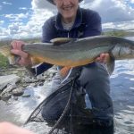 Happy angler holding a large rainbow trout during a fishing trip in a beautiful river landscape. Vibrant rainbow trout caught while fishing in a scenic river setting, showcasing freshwater fishing adventure.