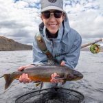 Happy female angler with fishing rod and caught fish in river, enjoying outdoor fishing adventure. Fish Partner angler holding a freshly caught fish in river setting, outdoor fishing with fishing gear and fly rod.