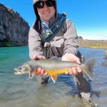 A fisherman proudly displays a freshly caught fish in a clear river with scenic cliffs, highlighting quality freshwater fishing. Healthy fish caught during outdoor fishing trip in pristine river environment.