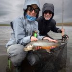 Fish partner, fly fishing, angling, catch and release, river fishing, outdoor activity, fishing enthusiasts, wild fish, scenic landscape, fishing rod, cloudy weather.
