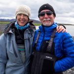 Smiling people enjoying fishing adventure in Iceland with waterproof jackets and scenic landscape background. Happy anglers in outdoor fishing gear near a water body in Iceland, wearing waterproof jackets and warm clothing.