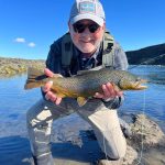 Beautiful outdoor fishing scene with a man showcasing his rainbow trout catch at the river. A man holding a freshly caught rainbow trout by a river, enjoying fishing outdoors on a sunny day.