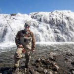 Fishing enthusiast enjoying a day of angling by a waterfall outdoors. Fishing enthusiast in front of a waterfall during a fishing trip.