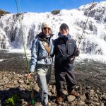 Happy anglers fishing near rushing waterfall with fishing equipment and outdoor gear in scenic landscape. Fishing couple by waterfall, outdoor fishing adventure with fishing rods, scenic river waterfall, happy anglers enjoying freshwater fishing trip, adventurous fishing excursion.
