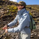 Woman fishing with rod outdoors, exploring nature in scenic wilderness for sport or leisure. Vibrant woman fishing in rugged outdoor landscape, enjoying nature and sport fishing adventure.