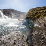 Enjoy fishing at Iceland's waterfalls with a professional angler casting in pristine river waters, surrounded by stunning natural scenery. Fishing in Iceland at a waterfalls river with a person casting a line and a scenic landscape.