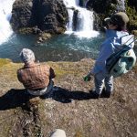 Two people fishing by a waterfall, capturing a serene outdoor fishing experience at Fish Partner. Fishing enthusiasts enjoying freshwater fishing near a scenic waterfall at Fish Partner.