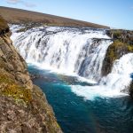Majestic waterfall flowing into turquoise waters amidst rugged terrain. Vibrant waterfall cascading over rocks in a scenic natural landscape.