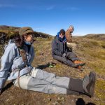 Enjoying a scenic fishing trip in Iceland's natural landscape with friends. Fishing enthusiasts relaxing on a mossy hillside near a waterfall in Iceland.
