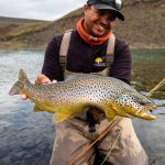 Trout fishing outdoor in nature with a smiling fisherman holding a large, healthy brown trout. Perfect for fishing and outdoor activity keywords. Vibrant brown trout caught during fly fishing in scenic mountain river. Man enjoying outdoor fishing adventure with fresh catch.