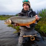 A fisherman displaying a large rainbow trout caught during a guided fishing trip in the wilderness with scenic natural surroundings. Big rainbow trout caught by angler in wilderness lake for fishing enthusiasts.