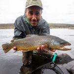 A smiling angler proudly displays a large rainbow trout he caught in the river. Vibrant rainbow trout caught during fishing trip in scenic mountain river.