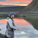 Fly fisherman standing next to a river at sunset