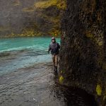 A person engaged in fishing along a volcanic canyon river, surrounded by rugged cliffs and vibrant waters. Fishing person on a rocky riverside in Iceland, catching fish with scenic moss-covered cliffs.