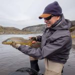 A man proudly displays a freshly caught brown trout in a pristine outdoor river setting. Vibrant brown trout caught during fishing trip in scenic river landscape.