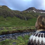 A woman with blonde hair gazing at scenic waterfalls and mountain views in Iceland, perfect for outdoor fishing and adventure trips. Fishing partner enjoying Icelandic waterfalls and scenic mountain landscape.