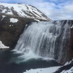 Stunning waterfall in a snowy mountain landscape, perfect for nature and outdoor adventure enthusiasts. Waterfall cascading over rocky cliffs with snow-capped mountains in the background, showcasing scenic natural beauty.