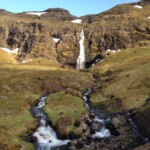 Scenic Icelandic landscape featuring a waterfall, stream, and lush green hills, perfect for trout fishing adventures. Fish partner Iceland trout fishing stream waterfall landscape.