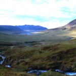 Beautiful Icelandic landscape featuring mountains, lush green valleys, and a winding river beneath a blue sky. Scenic valley with mountains and flowing river in Iceland.