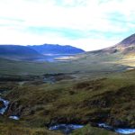Beautiful Icelandic landscape featuring mountains, lush green valleys, and a winding river beneath a blue sky. Scenic valley with mountains and flowing river in Iceland.