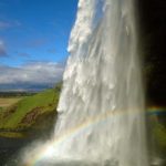 Scenic Icelandic waterfall with rainbow, lush green landscape, and blue sky, perfect for nature and travel enthusiasts. Viking Waterfall in Iceland with rainbow, lush greenery, and blue sky.
