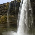 Scenic waterfall in Iceland with cascading water, rugged cliffs, and lush green surroundings showcasing natural beauty and outdoor exploration opportunities. Misty waterfall in Iceland cascading over rugged cliffs, lush green landscape, wide-angle view of natural wonder, outdoor adventure, scenic landscape.