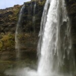 Scenic waterfall in Iceland with cascading water, rugged cliffs, and lush green surroundings showcasing natural beauty and outdoor exploration opportunities. Misty waterfall in Iceland cascading over rugged cliffs, lush green landscape, wide-angle view of natural wonder, outdoor adventure, scenic landscape.