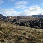 Iceland volcanic landscape with moss, rocks, and mountains under blue sky. Vast Icelandic volcanic landscape with moss-covered ground and rocky formations under a partly cloudy sky.