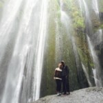 Large waterfall with visitors exploring the scenic environment and enjoying nature’s adventure. Majestic waterfall with two people standing near the base, surrounded by lush greenery and misty spray, capturing nature's beauty.