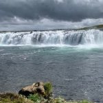 Scenic waterfall in a lush, natural environment, perfect for aquatic life and water source discussions. Waterfall over a river with lush greenery and cloudy sky, showcasing natural aquatic scenery.
