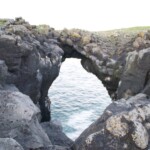 Natural sea arch formed by volcanic rocks along the Icelandic coast, offering stunning ocean views and rugged coastal scenery. Rock formation with a natural sea arch, coastal scenery, volcanic rocks, ocean view, Icelandic landscape, Fish Partner.