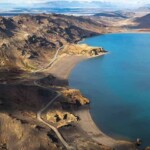 A scenic view of a large water reservoir near volcanic terrain, supporting fish farming and aquaculture industries. Lake with surrounding mountains and a winding road, illustrating water facilities for sustainable aquaculture.