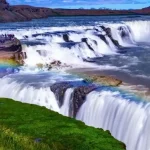 Scenic waterfall with rainbow, lush landscape, and flowing water, showcasing natural beauty perfect for fish and aquaculture enthusiasts. Vibrant waterfall with lush greenery and rainbow at FishPartner.com.
